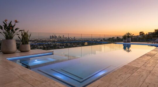 Luxury infinity pool with glass edge overlooking a city skyline at sunset