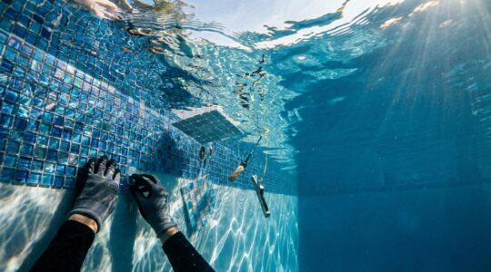 Professional installing glass mosaic tiles underwater in pool with specialized tools